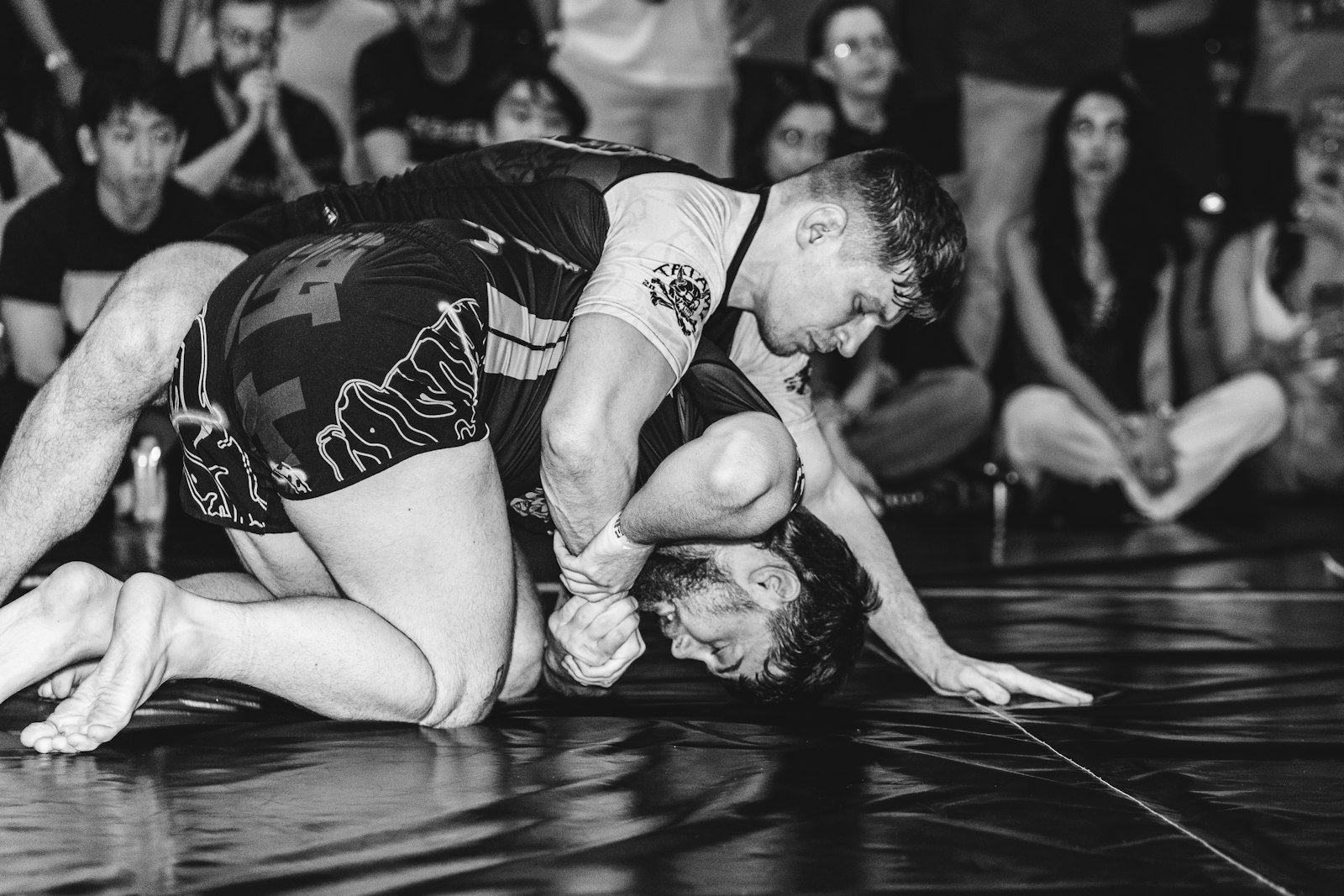 Two men grappling on a mat with spectators watching.